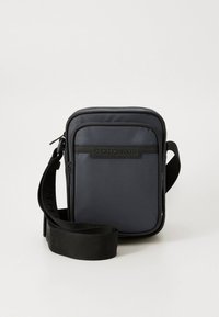 Must nylonist risti kehapüüdja kandekott ristkülikukujuline, reguleeritava rihma ja esiküljel reljeefse logoga. Omab sileda viimistlusega ja tõmblukuga sulgemist.