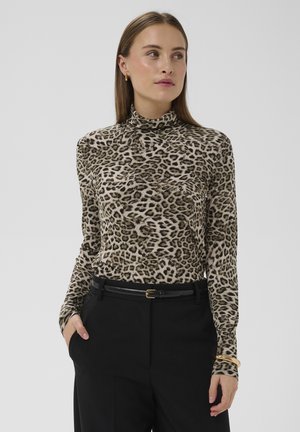 Langärmeliges Oberteil mit Leopardenmuster und hohem Kragen, aus weichem Stoff. Kombiniert mit schwarzer Hose und einem schlanken schwarzen Gürtel.