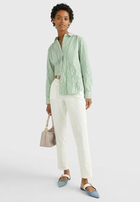 Camicia a righe verde e bianca a maniche lunghe, vestibilità rilassata. Pantaloni bianchi, ballerine a punta blu e bianche, e una borsa beige.