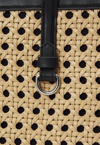 Tkaný béžový materiál s černým koženým páskem a stříbrnými kovovými doplňky. Má texturovaný vzor a kruhový kovový kroužek jako dekoraci.