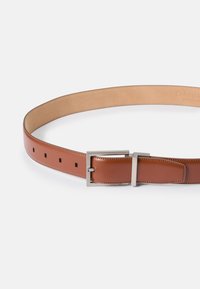 Cintura in pelle marrone con una finitura liscia, fibbia rettangolare in argento e fori regolabili con accenti quadrati lungo la cinghia.