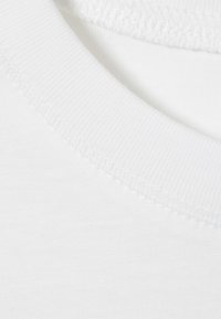 Weißer Baumwollstoff mit glatter Textur, ausgestattet mit einem gerippten Rundhalsausschnitt. Die Nähte sind ordentlich und gleichmäßig verteilt.