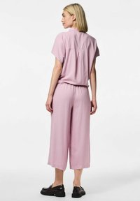Camisa corta de manga larga en rosa claro, metida dentro de unos culottes amplios a juego. Unos zapatos planos negros completan el look. Textura suave y ajuste relajado.