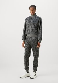 Leopardmønstret treningsdrakt i dempede gråtoner, med en glidelåsjakke med ribbede mansjetter og matchende joggebukser med ankelmansjetter.