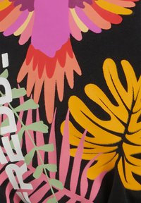 Musta kangas, jossa on värikäs kukkakuosi, jossa on vaaleanpunaisia, oransseja ja keltaisia yksityiskohtia; sisältää rohkeaa valkoista tekstiä ja vihreitä lehtiä.