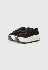 Sorte plattform sneakers med en teksturert stoffoverdel, hvit mellom såle, og slitesterk svart gummisåle med et sikksakkmønster.