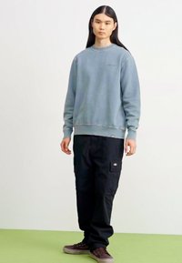 Lichtblauwe sweatshirt met ronde hals en geribde mouwen, gecombineerd met zwarte cargo broeken met zakken en bruine schoenen.