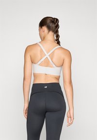 Svetlo siva športna modrček z križnimi naramnicami, gladko teksturo in prilagodljivimi zaklepi; v kombinaciji s črnimi visokim pasom legicami.