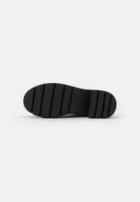 Suela de zapato de goma negra con ranuras horizontales para tracción, forma redondeada y diseño plano. Textura suave sin patrones ni acentos visibles.