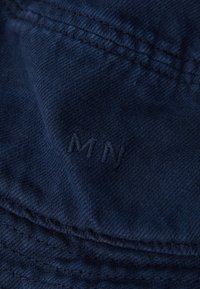 Navy bucket hat made of soft fabric, featuring stitched accents and embossed "MN" logo. Texture appears smooth with minimal sheen.