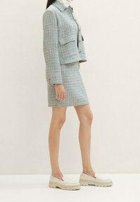 Completo in due pezzi in tessuto texturizzato di un azzurro chiaro. Una giacca corta con tasche a toppa abbinata a una gonna aderente. Mocassini bianchi chunky completano il look.