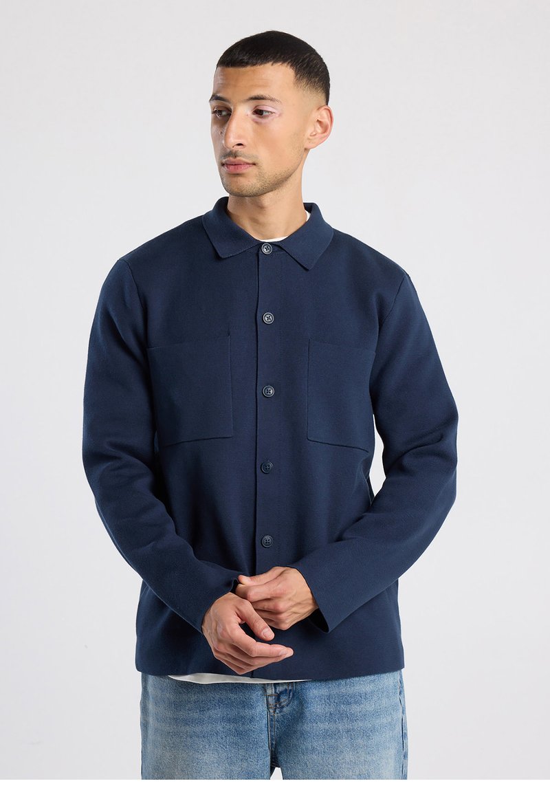 Marineblauw overhemd met knopen, gemaakt van zachte stof, met een kraag, twee borstzakken en lange mouwen. Details van de gestructureerde stof zichtbaar.