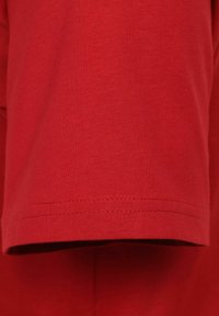 Czerwony bawełniany materiał koszulki wyświetlony, z gładką fakturą, prostym wykończeniem rękawów oraz prostym wzornictwem bez nadruków czy akcentów.