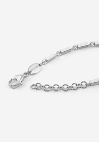 Bracciale in argento con maglie rettangolari e tonde, dotato di chiusura a gabbiano e di un'etichetta con marchio incisa con "GUESS". Texture liscia.