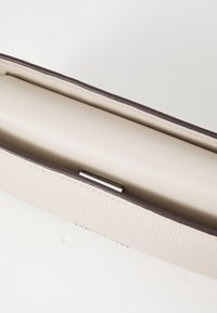 Texturerad krämfärgad läderväska med en slät beige insida, med mörkbruna detaljer och en metallklämma som stängning.