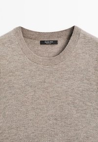 Beige neule, jossa on pyöreä kaula-aukko, ribbireunat ja hihansuut, valmistettu teksturoidusta kankaasta. Tunnuksessa lukee "Massimo Dutti, valmistettu Kiinassa."