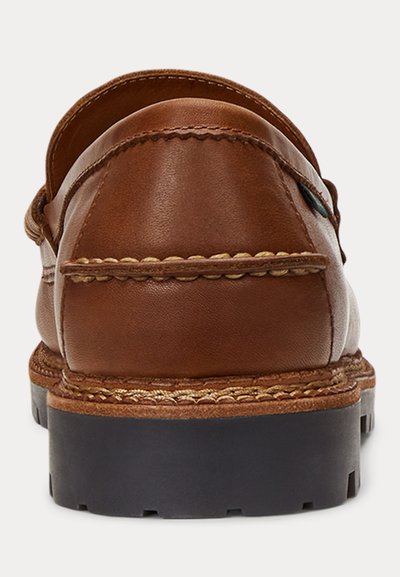 Ruskea nahkainen loafer, jossa yksityiskohtaiset ompeleet ja paksu musta kumipohja, valkoisella taustalla takaa kuvattuna.