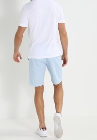 Shorts en coton bleu clair à coupe droite avec poches latérales, associés à une chemise blanche à manches courtes et des baskets blanches.