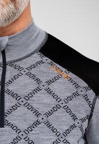 Grå og sort pullover med lynlås krave, der har en mønstret tekstur med gentagne "DOVRE"-ord og et orange logo på skulderen.
