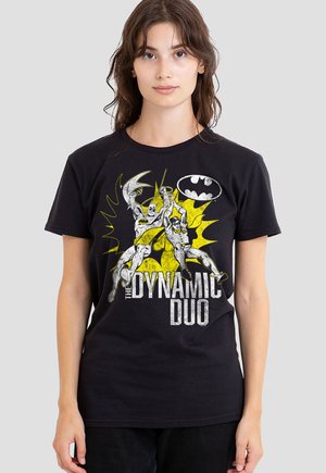 Woman wearing a black T-shirt with a vintage Batman and Robin graphic and the text "The Dynamic Duo" in white and yellow colors.