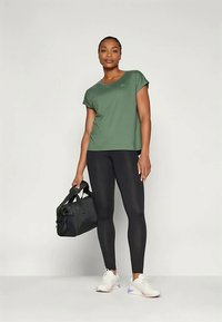 Top sportivo verde a maniche corte abbinato a leggins neri. Include anche sneakers bianche con dettagli viola e una borsa da palestra nera.