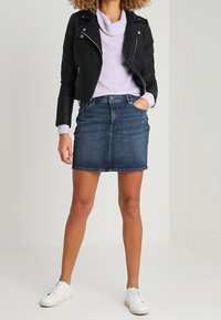 Czarna skórzana kurtka motocyklowa, lawendowy sweter z kopertowym dekoltem, niebieska dżinsowa spódniczka mini i białe sneakersy. Swobodny, dopasowany krój.