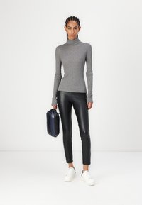 Hallide hall turtleneckiga pluus pikkade varrukatega, mis on kombineeritud mustade kunstnahast retuusidega ja valgete tossudega. Hoides tumehallis kotis.