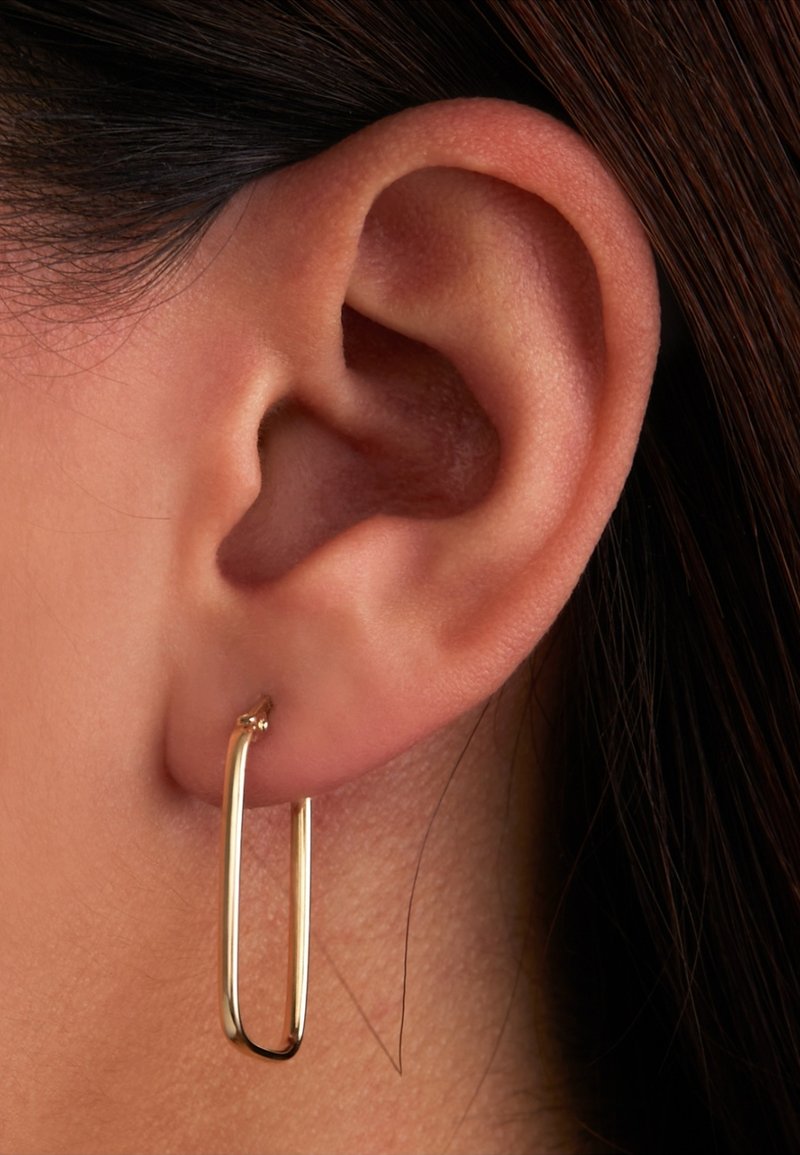 Boucles d'oreilles en or en forme d'ovale allongé, avec une surface lisse et brillante et un design minimaliste, fixées à un lobe d'oreille percé.