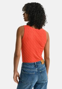 Oranje kabelgebreide mouwloze top met een ronde hals, gecombineerd met hooggetailleerde blauwe denim jeans met achterzakken en een merketiket.