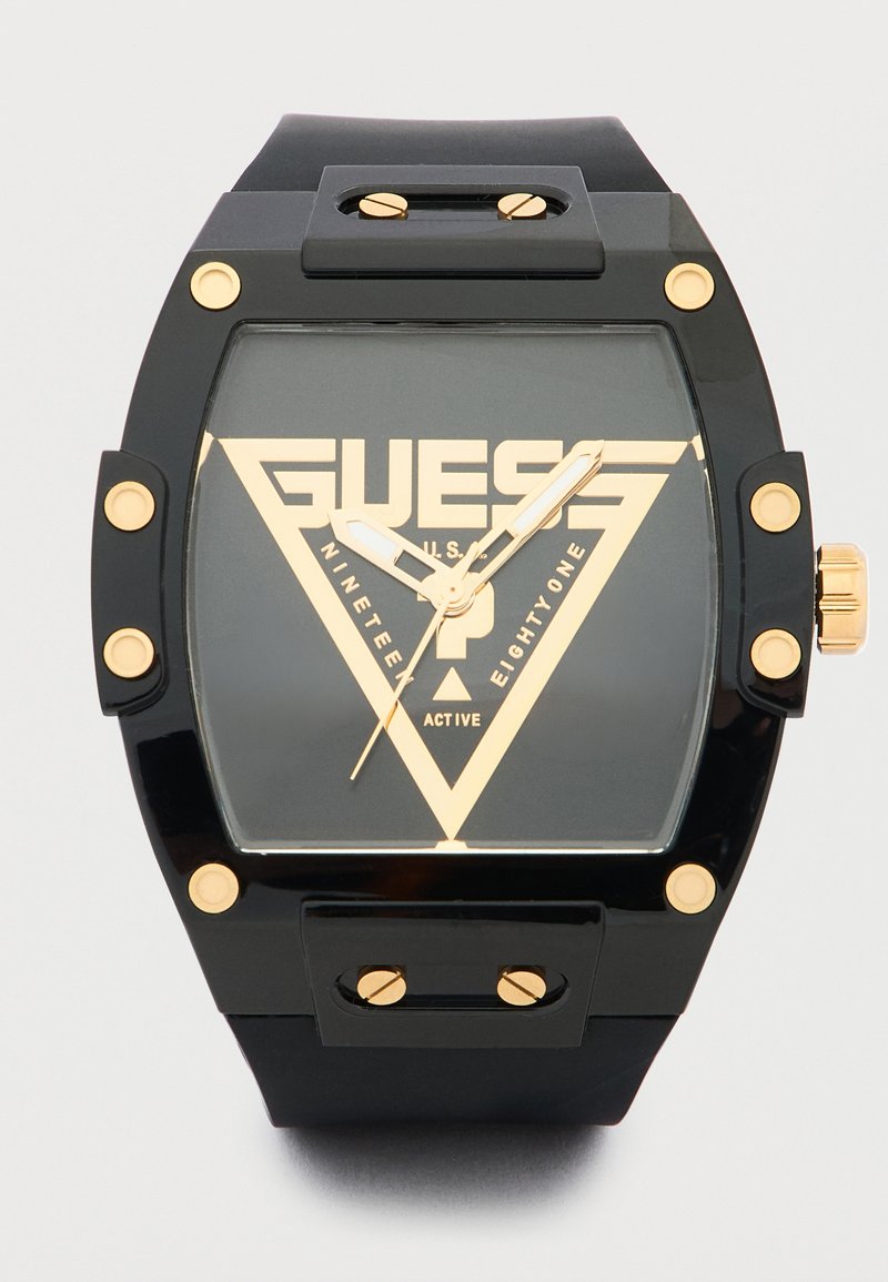 Μαύρο και χρυσό ρολόι χειρός Guess με τετράγωνο καντράν, χρυσούς βιδωτούς στεφάνους και έντονο τριγωνικό λογότυπο στο καντράν.