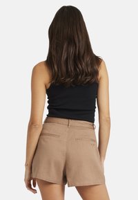 Ruskeat pellavasekoitetut shortsit, joissa on keskikorkea vyötärö, etupocketsit ja takapocketsit. Musta toppi kontrastina, malli kääntynyt pois katsojasta.