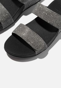 Zwarte sandalen met sprankelende grijze textiele banden, voorzien van een dikke, gevoerde zool. De banden hebben een gladde textuur en glinsterende details.