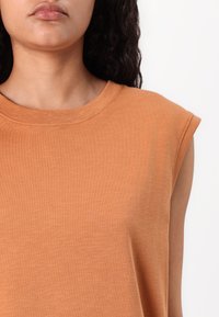 Haut orange à manches courtes avec un col rond et un tissu doux et texturé. Épaules accentuées avec une coupe décontractée.