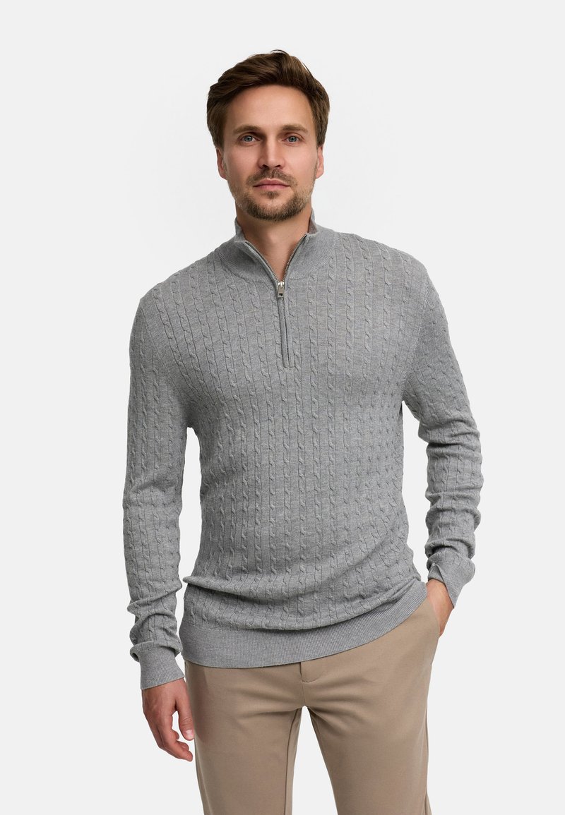 Grå kabelstrikket genser med glidelås i kragen, tettsittende design, ribbede mansjetter og kant, kombinert med beige bukser.