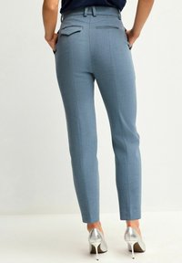 Helleblaue maßgeschneiderte Hose mit schlanker Passform, ausgestattet mit Gesäßtaschen und flachem Vorderteil. Kombiniert mit silbernen High Heels.