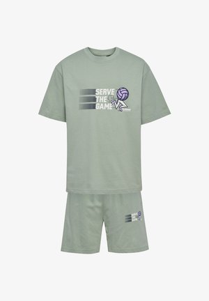 Dwoje dzieci noszą dopasowane szarozielone szorty i koszulki z napisem „Serve the Game”, fioletową grafiką siatkówki, białe skarpetki i różowe trampki.