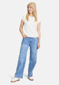 Hvid kortærmet top med struktureret mønster, parret med lysblå viddejeans og hvide sneakers med brune såler.