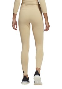 Leggings beige con un tessuto liscio ed elastico. Vita alta, design aderente e dettagli di texture sottili. Calzature nere con suole spesse.