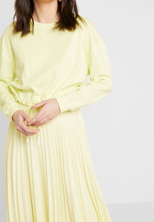 Sweat-shirt jaune clair à coupe décontractée et manches longues, associé à une jupe plissée assortie avec une taille à cordon.