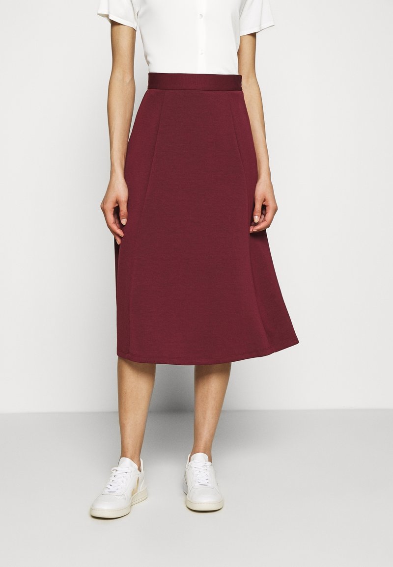 Burgundy midi-hame pehmeässä jersey-kankaassa, jossa on istuva vyötärö ja A-linjainen siluetti, yhdistettynä valkoisiin lenkkareihin.