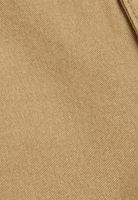 Tela de color beige con una superficie lisa y ligeramente texturizada que presenta estrías diagonales paralelas. El material es duradero y consistente en color.