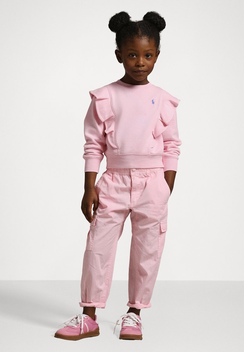 Rosa sweatshirt med volanger, broderad logotyp; matchad med rosa cargobyxor och rosa sneakers med vita snören och bruna sulor.