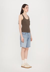 Top in cotone marrone a costine, pantaloni corti in denim blu con orlo sfrangiato, calzini bianchi, scarpe da ginnastica beige con strisce colorate. Il modello è in posizione laterale.
