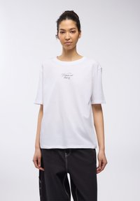 T-shirt bianco a maniche corte in cotone con scollatura rotonda. Presenta una scritta nera in corsivo "Se sei fuori quel giorno" sul petto. Vestibilità comoda.