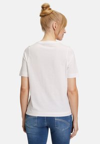 T-shirt bianca in cotone con maniche corte, scollatura rotonda e vestibilità comoda. Abbinata a jeans in denim blu chiaro. Design semplice, senza motivi.