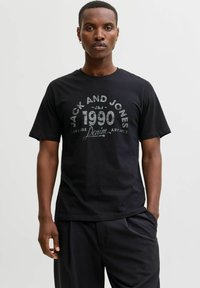 Juodas medvilnės marškinėliai su apvali apykakle ir trumpomis rankovėmis, su pilku grafiniu dizainu, kuriame yra "JACK AND JONES" ir "1990."