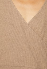 Beige ribbat tröja med djup V-ringning, som har överlappande paneler och en slät textur.