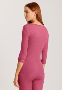 Top rosa a costine con maniche a tre quarti orlate in pizzo, scollo rotondo e silhouette aderente, abbinato a pantaloni coordinati.