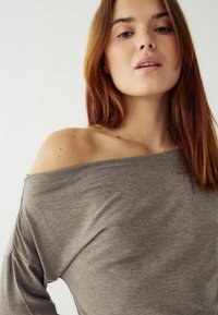 Pelēka, ar pleciem brīva augšdaļa, izgatavota no viegla auduma ar mīkstu tekstūru. Raksturīgas smalkas veidojuma detaļas un brīva piegriezuma formas.