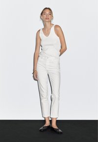 Bílý top bez rukávů v kombinaci s bílými džíny vysokého pasu a černými balerínami. Hladká tkanina a štíhlý střih s jemnou texturou. Jednoduchý, moderní design.